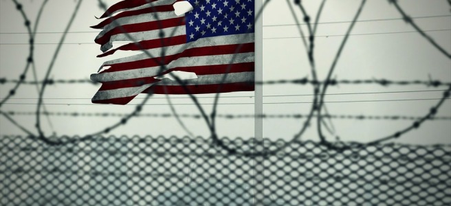 close-up picture tattered American flag behind barbed wire fence