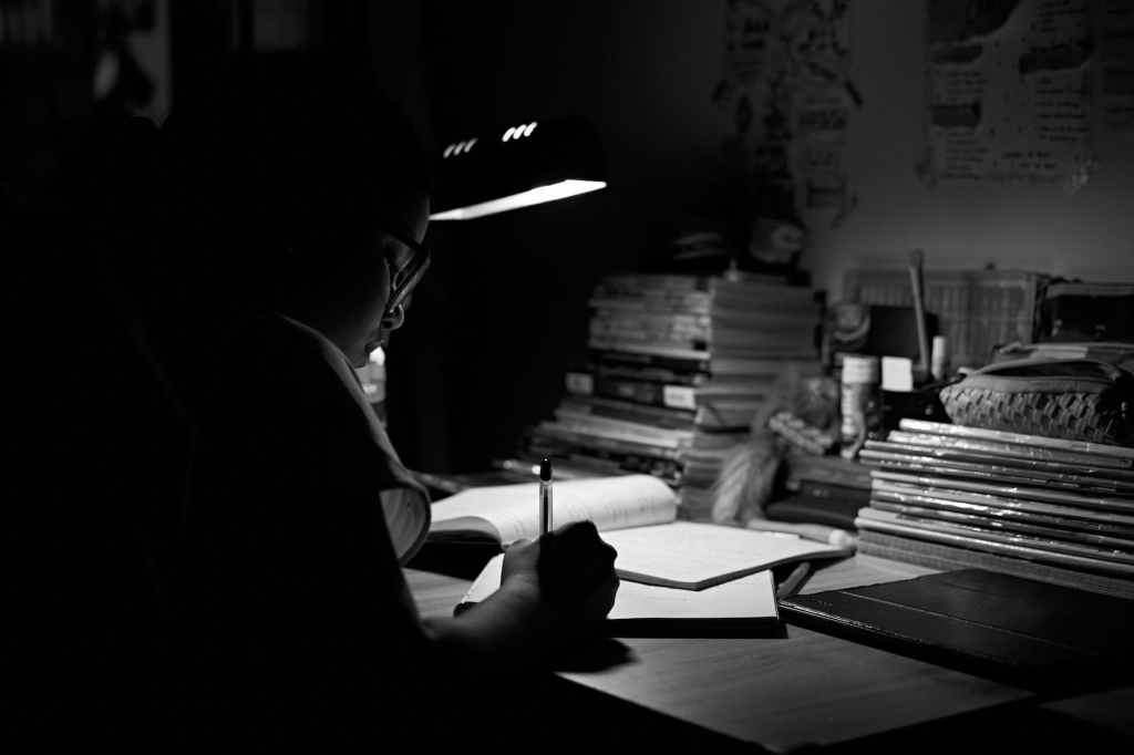 a woman with eyeglasses writing on white paper under a light