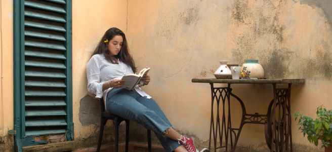 woman in white long sleeve shirt and blue denim jeans sitting on black wooden chair and reading a book