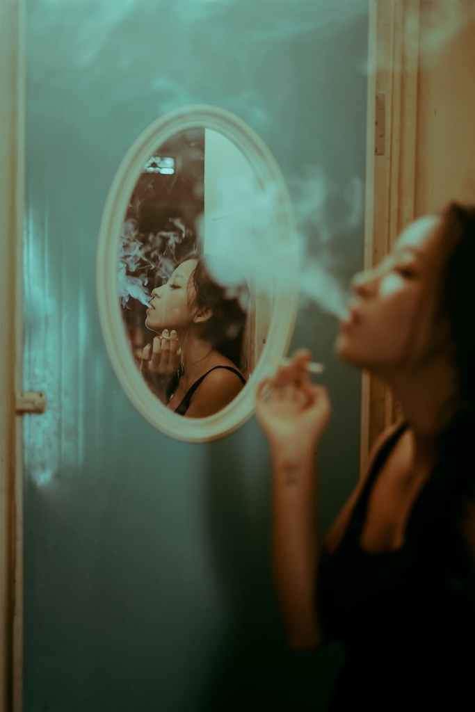 a reflection of a woman in the mirror smoking a cigarette