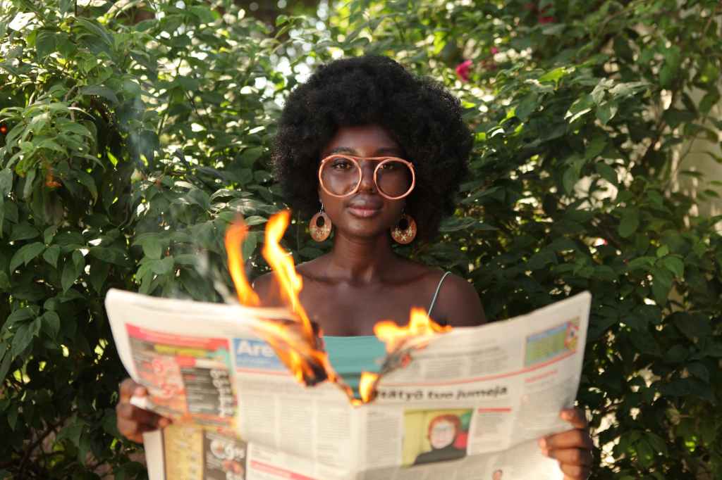 trendy black woman reading burning newspaper in garden