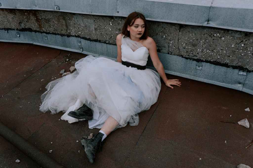 woman in white dress and black boots sitting on a concrete floor