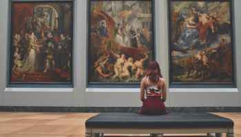 woman sitting on ottoman in front of three paintings