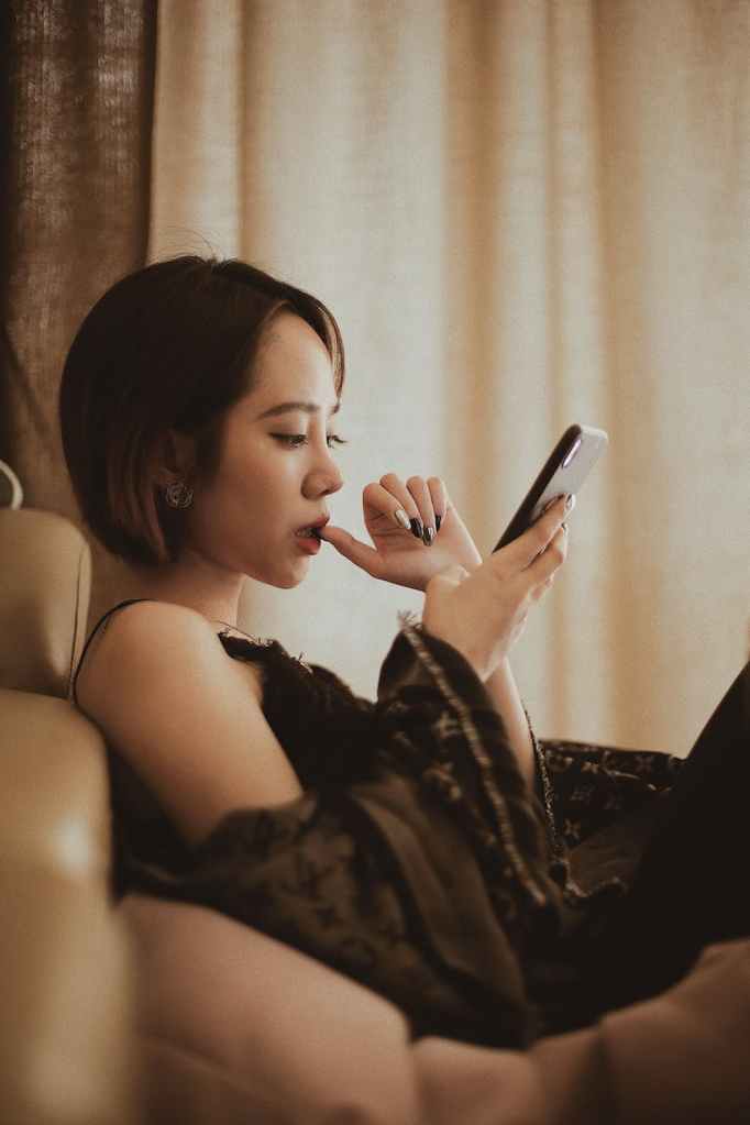 woman sitting on couch, biting thumb, and looking at cellphone