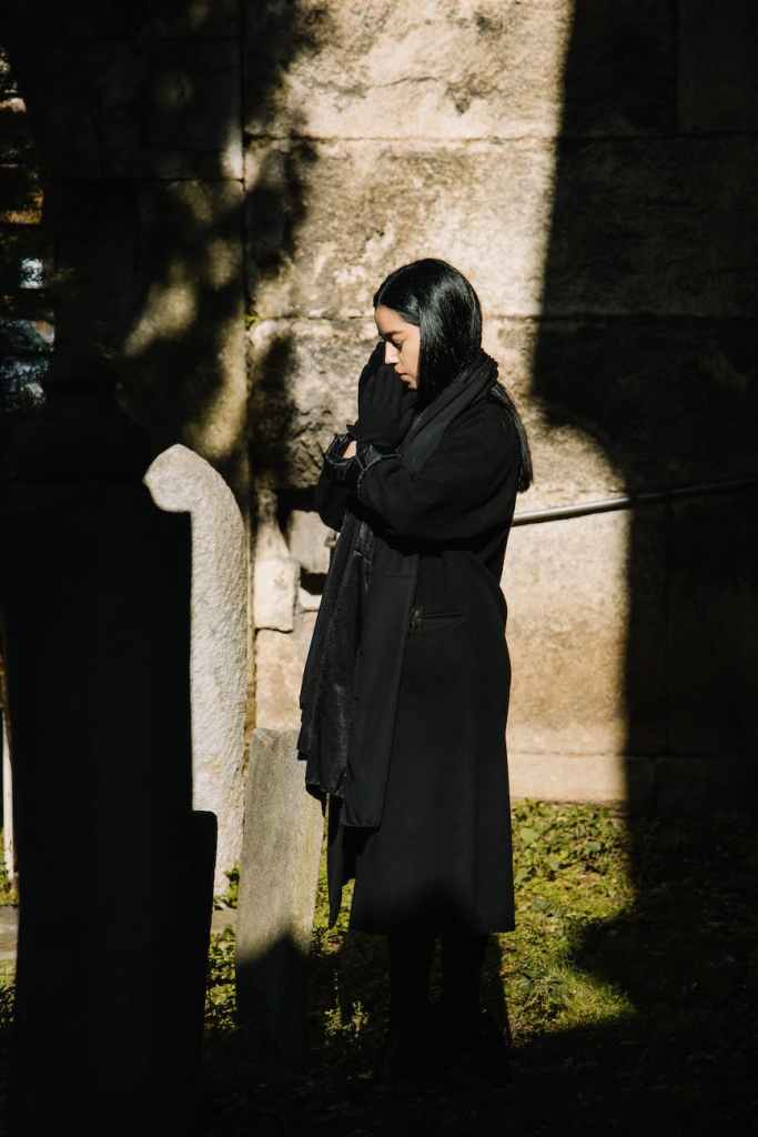 woman standing near gravestone and praying for deceased